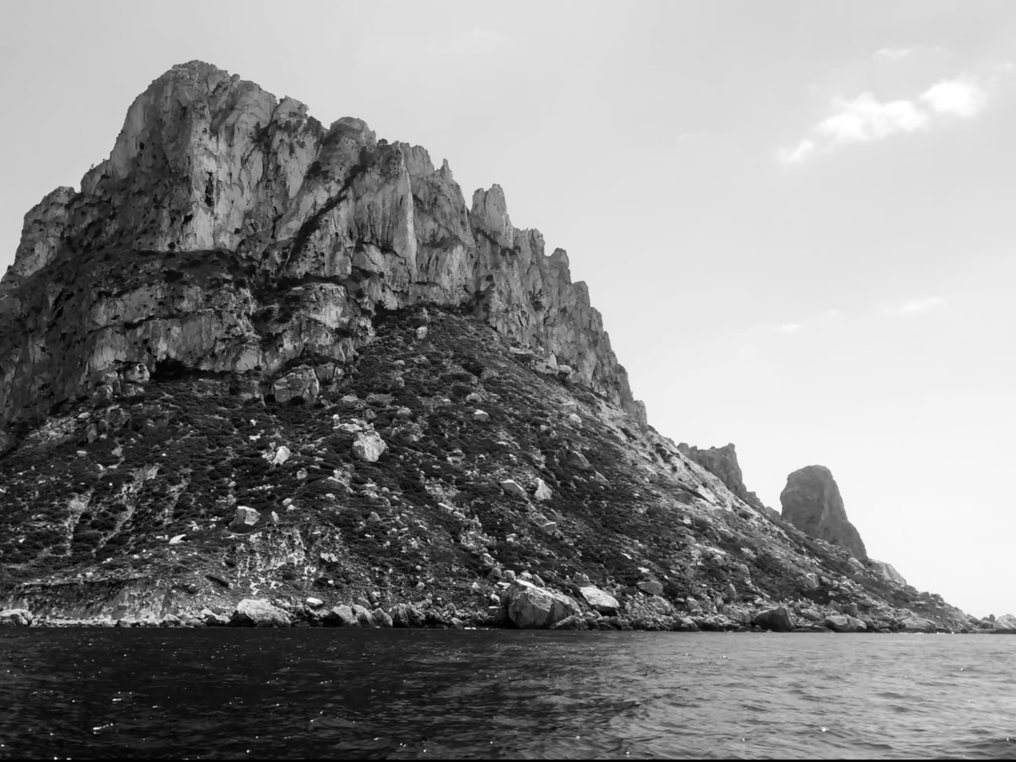 A rock mass rising straight out of the sea, its seaward face in shadow.